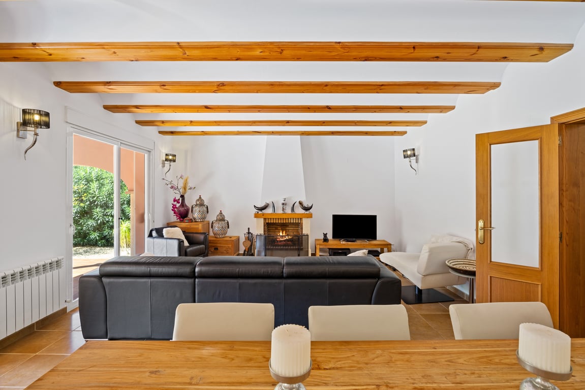 Salón luminoso con techos de vigas de madera, chimenea central de obra y acceso directo a la naya mediante puertas correderas de cristal. Suelos cerámicos y calefacción por radiadores.