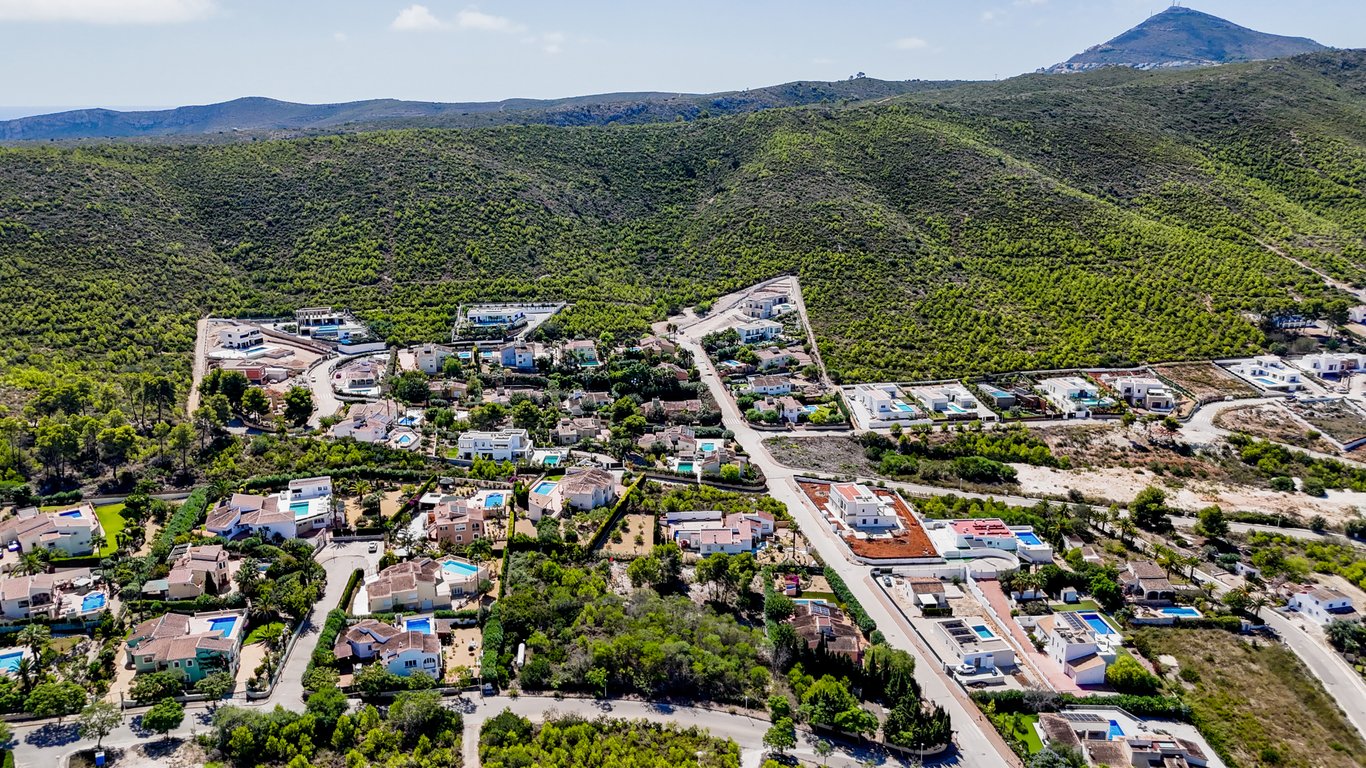 Vista aérea de la urbanización en Jávea, mostrando la tranquila ubicación de la villa rodeada de colinas verdes y paisajes mediterráneos.