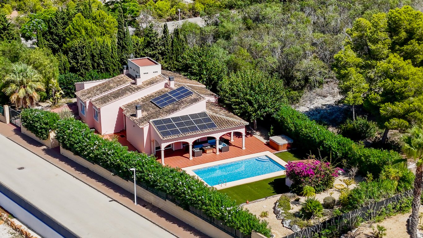 Vista aérea de la villa con paneles solares, piscina privada y naya arqueada, rodeada de vegetación mediterránea y una parcela totalmente vallada.