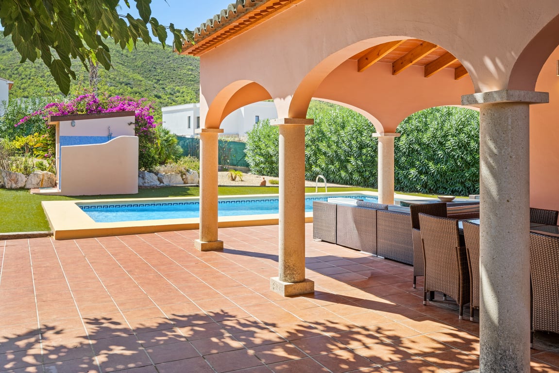 Amplia naya con arcos y columnas de piedra, suelo de terracota y vistas directas a la piscina de mosaico y las montañas de Jávea.