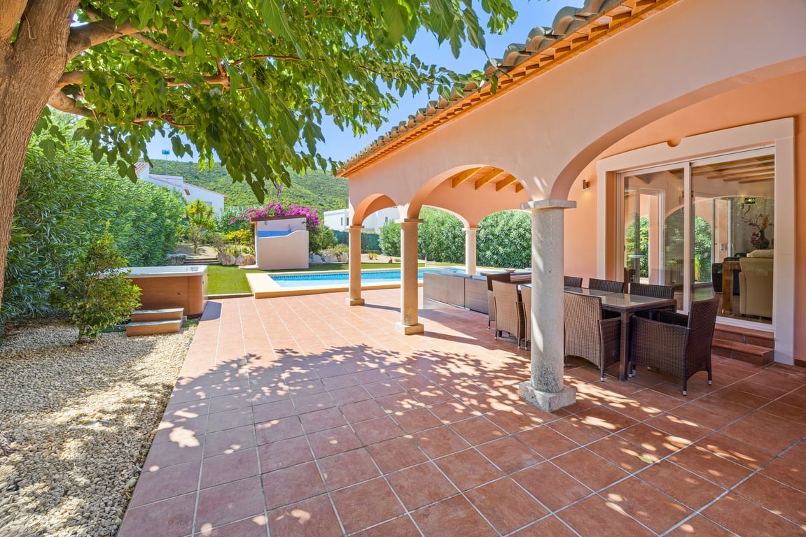 Naya cubierta con arcos, columnas de piedra y vigas de madera, equipada con comedor exterior frente a la piscina, jacuzzi y jardín con vistas a la montaña.