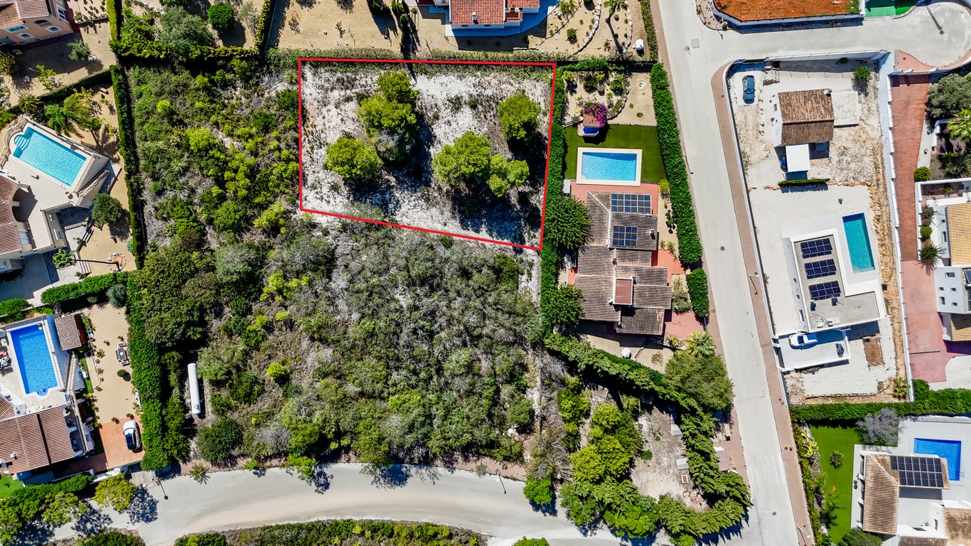 Vista aérea de la villa con paneles solares y piscina, destacando la parcela urbana edificable adyacente delimitada en rojo.