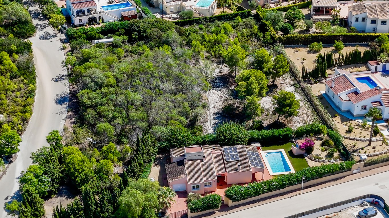Vista aérea que muestra la villa con paneles solares, piscina privada y la amplia parcela urbana adyacente con vegetación autóctona en Jávea.