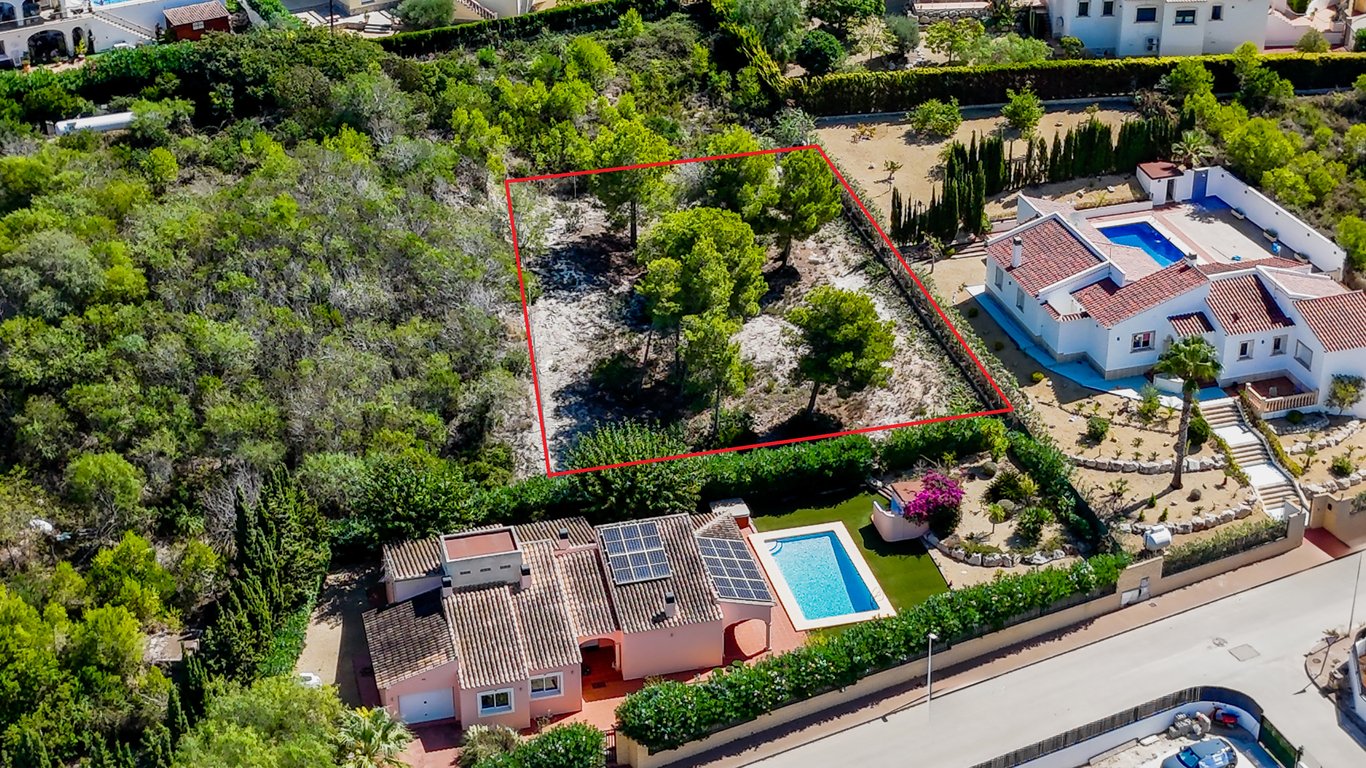 Vista aérea que muestra la villa con paneles solares y piscina, junto a la parcela urbana colindante de relieve llano y arbolado, delimitada en rojo.