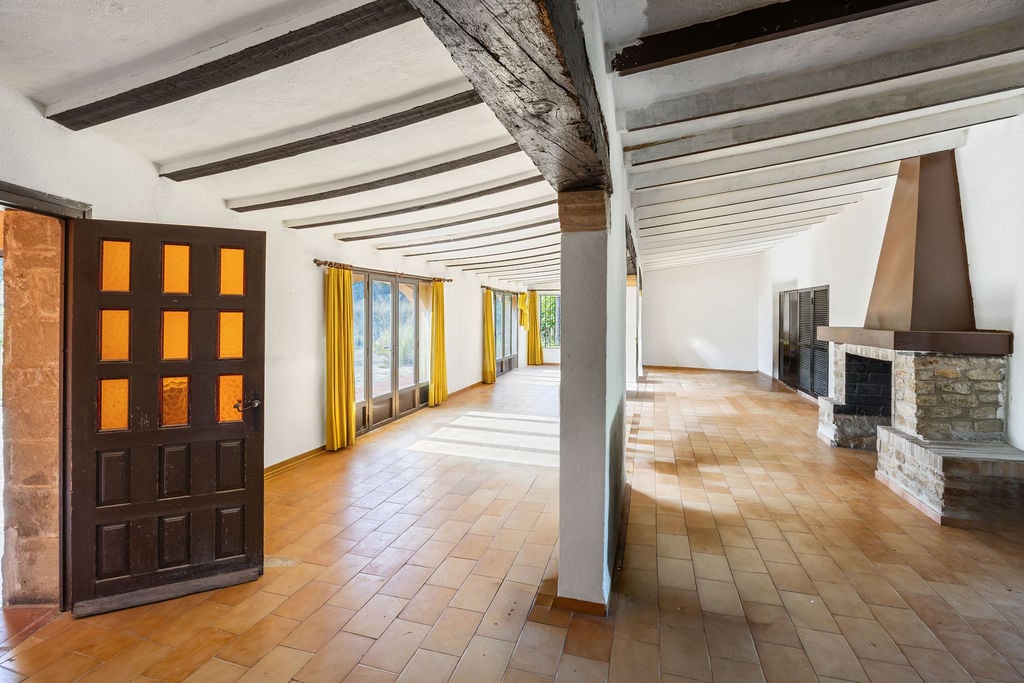 Amplio salón de estilo rústico con vigas de madera vista, suelos de terracota y una chimenea de piedra natural con campana metálica.