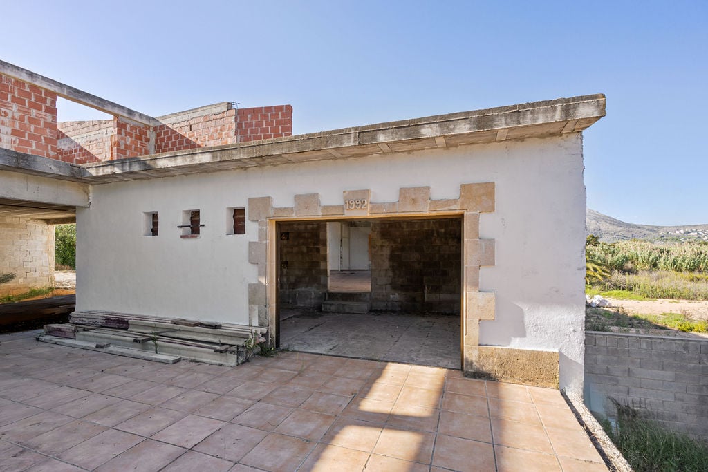 Estructura de obra con terraza de baldosas cerámicas, muros con detalles en piedra tosca y fecha de 1992 inscrita sobre el acceso principal.