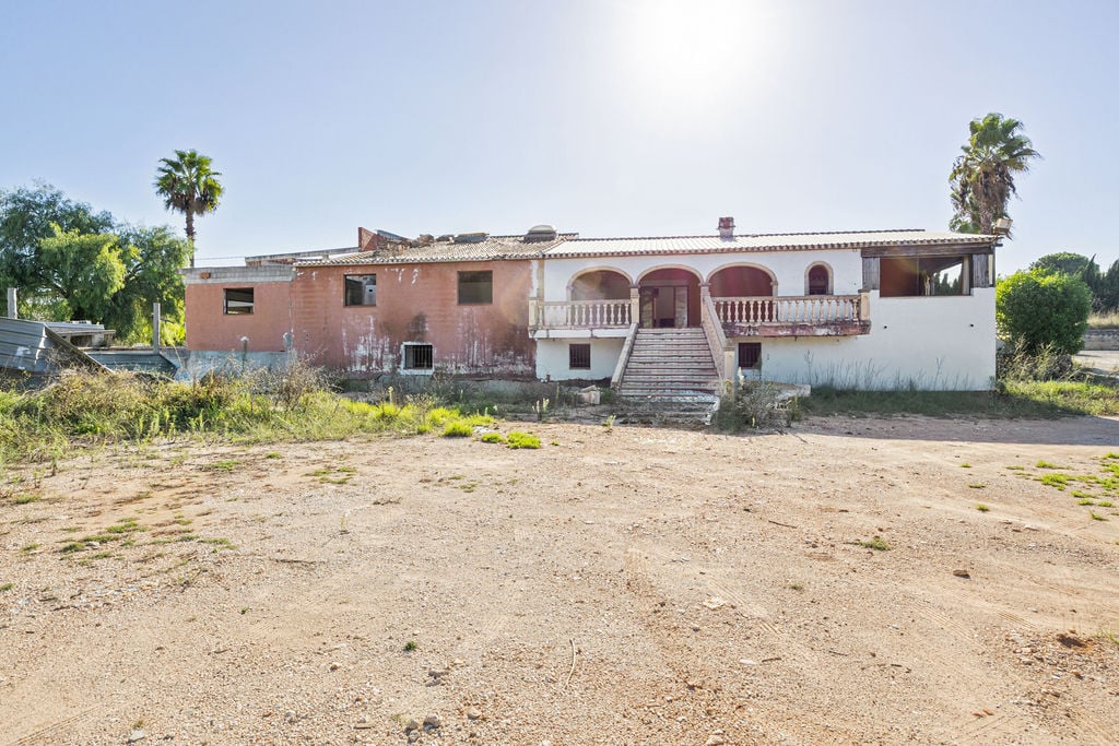Fachada principal de la construcción existente con arquería tradicional, balaustrada de piedra y escalinata central sobre una extensa parcela de terreno natural.