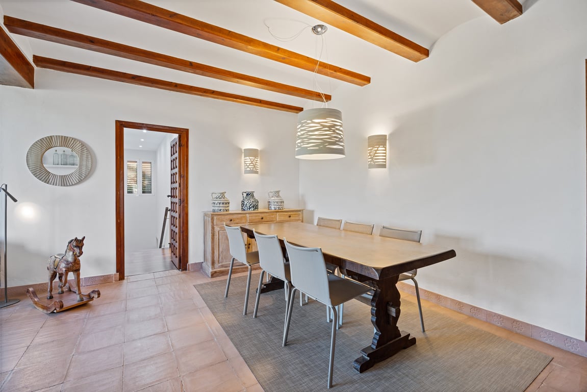 Comedor con vigas de madera vistas, suelo de baldosa cerámica artesana y mesa de madera maciza, iluminado por lámparas de diseño contemporáneo.