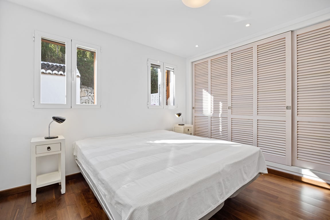 Dormitorio luminoso con suelos de madera, paredes blancas y un gran armario empotrado con puertas correderas de lamas. Incluye ventanas de doble acristalamiento y focos empotrados.
