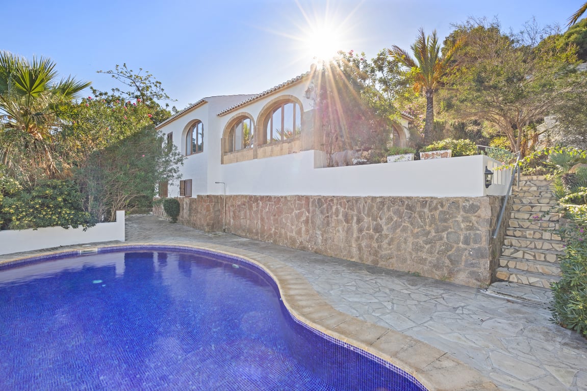 Exterior de la villa con piscina privada, muros de piedra natural y naya con arcos de piedra Tosca bajo el sol mediterráneo.