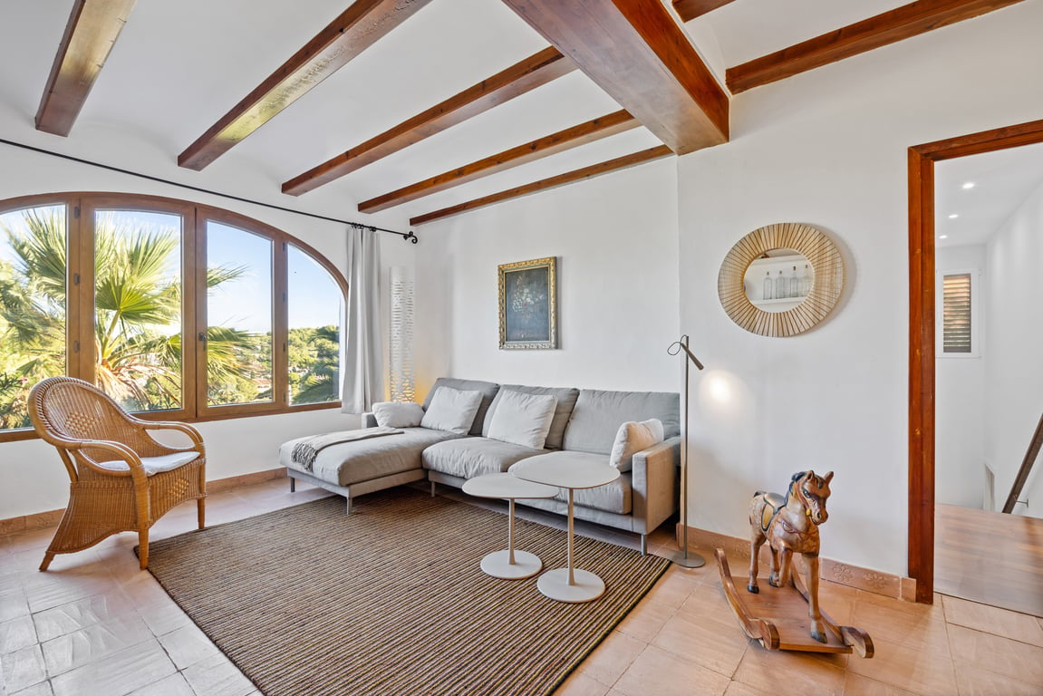 Salón luminoso con vigas de madera vista, suelos de baldosa artesana y un gran ventanal en arco con vistas al jardín mediterráneo.