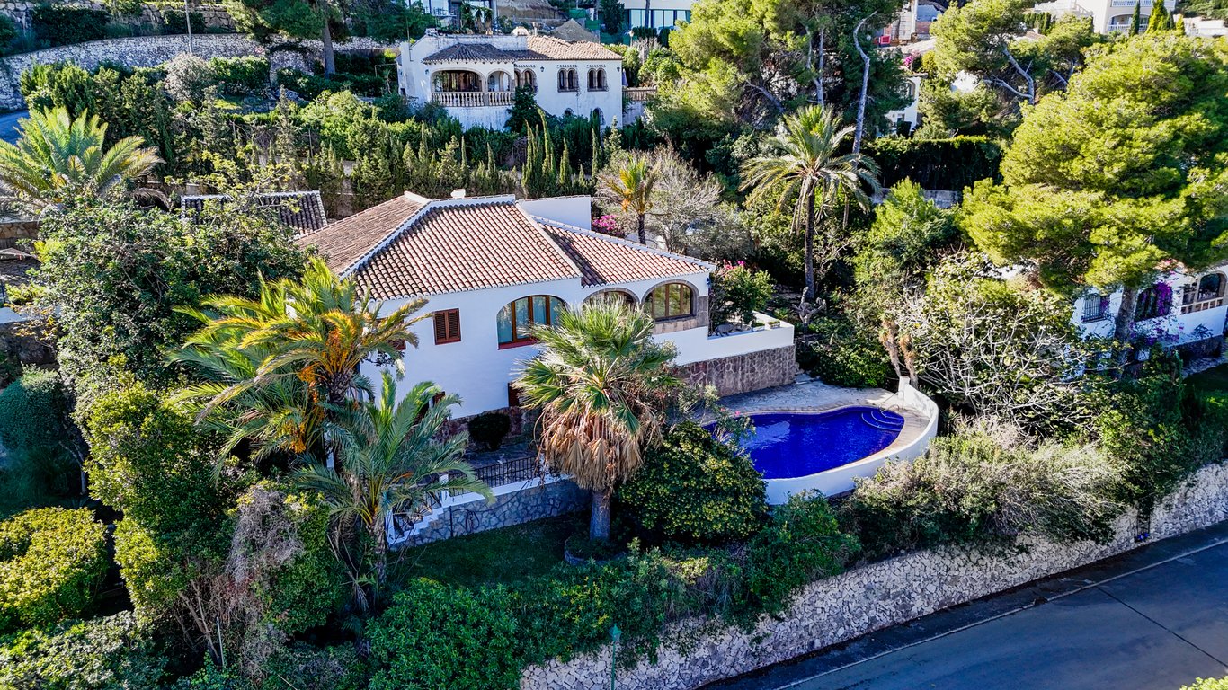 Vista aérea de la villa con arquitectura tradicional, destacando la piscina privada, la naya con arcos y el jardín mediterráneo rodeado de muros de piedra natural.