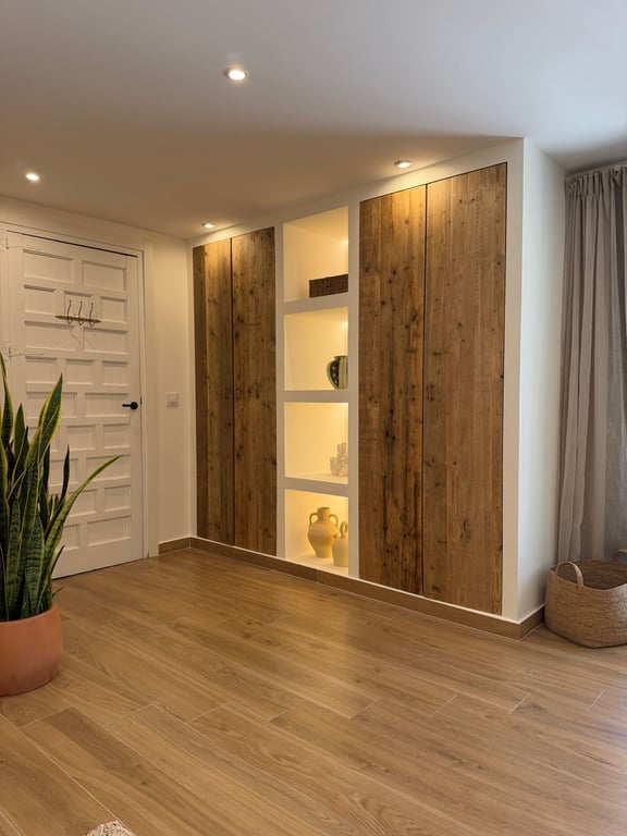 Armario empotrado de diseño rústico con puertas de madera natural y estanterías centrales integradas con iluminación LED sobre suelo cerámico de efecto madera.