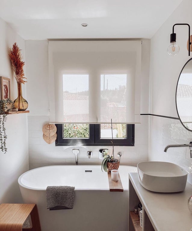 Baño de diseño con bañera exenta, lavabo sobre encimera y ventana de marco negro. Combina azulejos tipo metro blancos con cálidos detalles en madera natural.