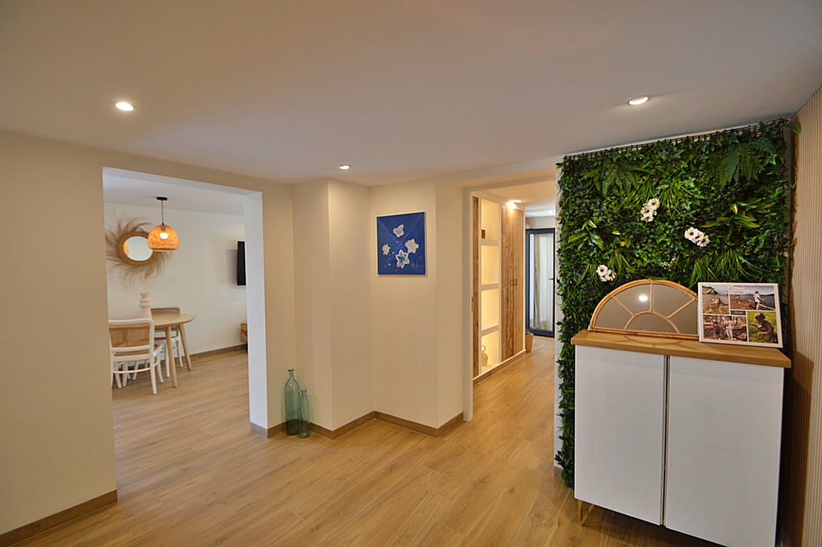 Distribuidor luminoso con suelos de madera, iluminación empotrada y un jardín vertical decorativo junto a un aparador moderno que conecta con el comedor.