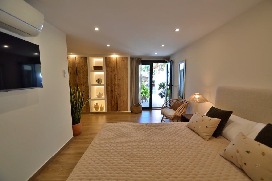 Dormitorio luminoso con armarios de madera natural, estanterías integradas con iluminación LED, suelos de gres efecto madera y acceso directo al jardín.