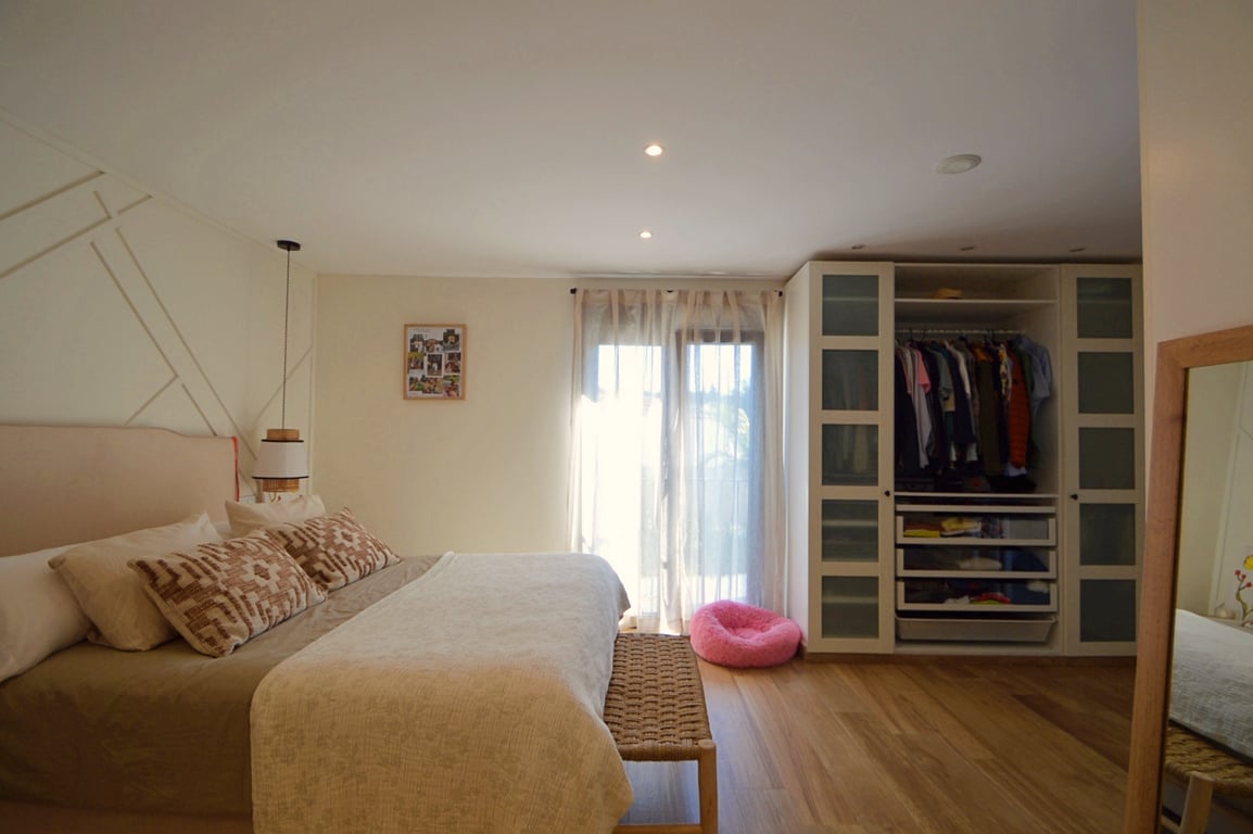 Dormitorio luminoso con suelos de madera, pared decorativa con molduras geométricas y armario empotrado con puertas de cristal translúcido y estanterías.