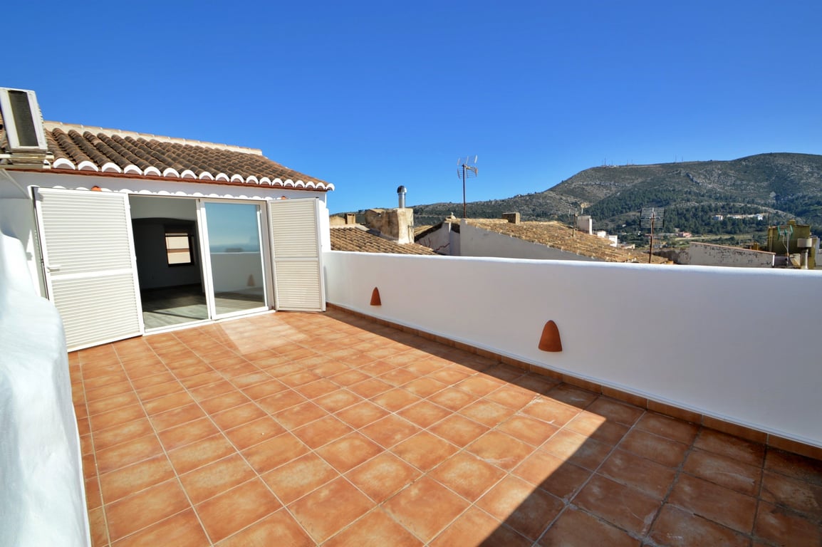 Amplia terraza en la azotea con suelo de baldosas de terracota, muros blancos y vistas despejadas a las montañas bajo un cielo despejado.