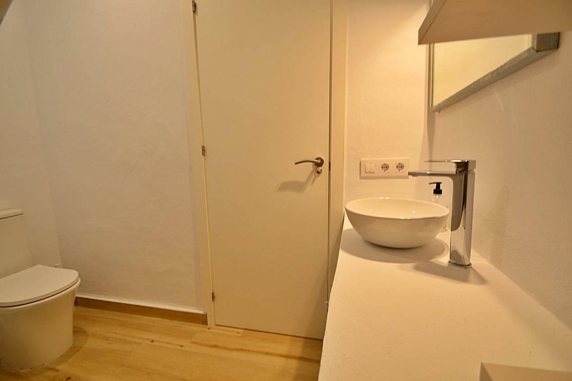 Cuarto de baño moderno con lavabo de sobremesa circular, grifería cromada y suelos de madera clara. El diseño minimalista incluye paredes blancas y sanitarios contemporáneos.