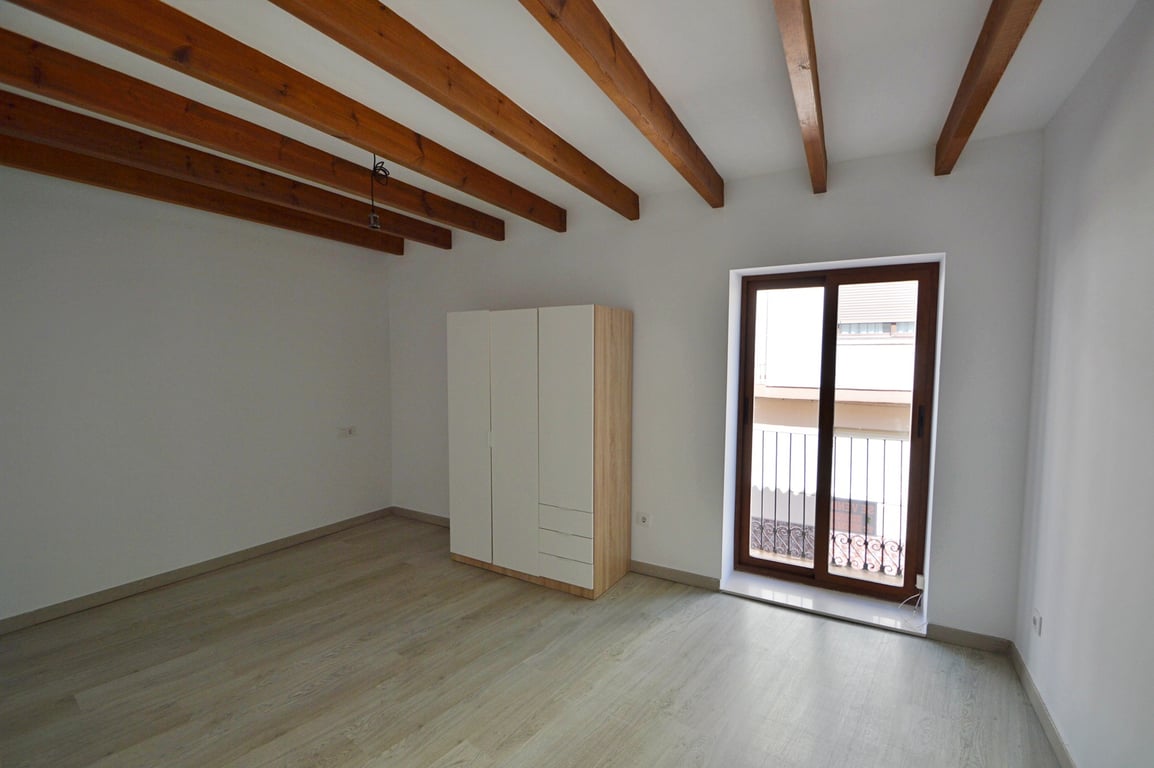 Dormitorio con vigas de madera a la vista, suelos de tarima clara y armario moderno. Dispone de acceso directo a un balcón privado mediante puertas correderas.