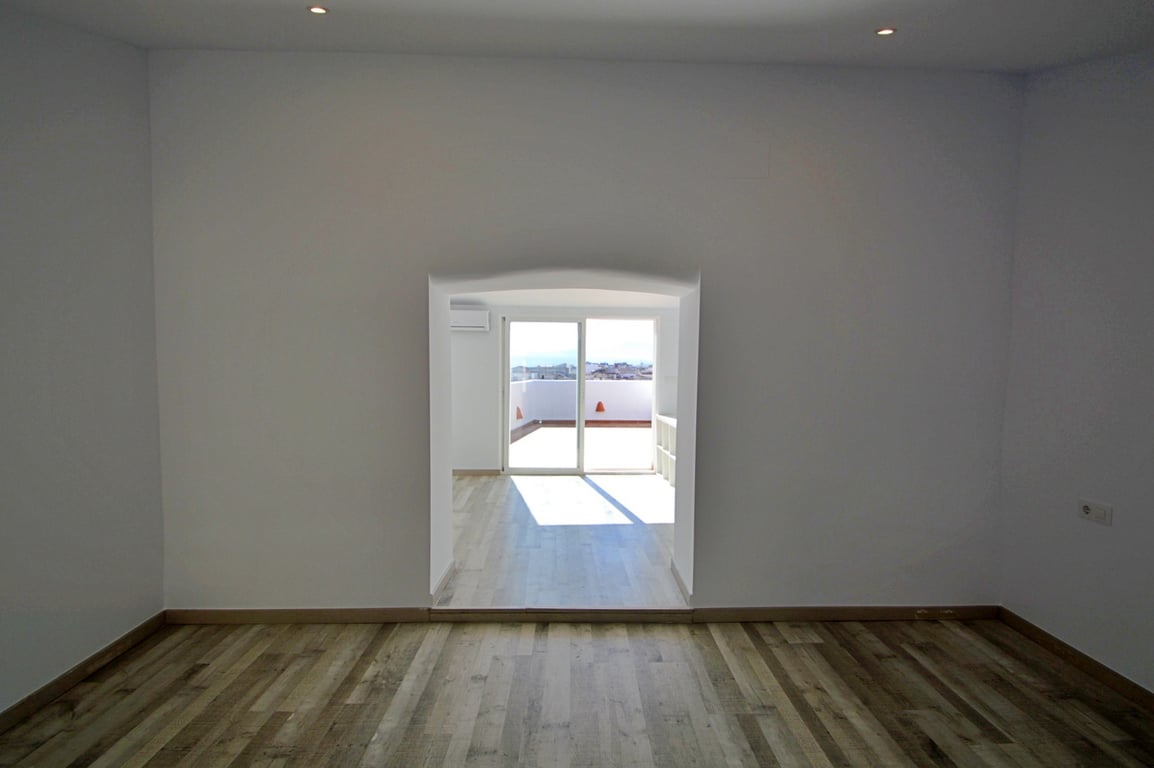 Estancia versátil con suelos de madera, iluminación empotrada y un arco que conecta con una zona luminosa con acceso directo a la terraza.