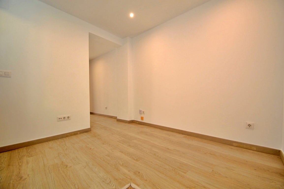 Habitación versátil recientemente renovada con suelos de tarima clara, paredes blancas lisas e iluminación mediante focos empotrados.