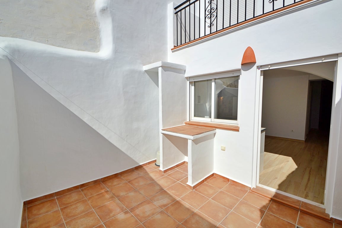 Patio privado con suelos de terracota, paredes blancas tradicionales y una zona de encimera exterior. Incluye acceso directo al interior y vistas al balcón superior.