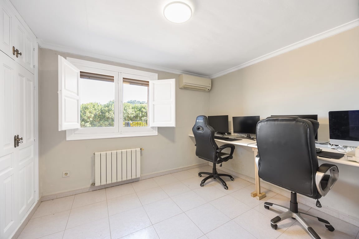 Despacho luminoso con armarios empotrados, aire acondicionado y calefacción. La ventana con contraventanas ofrece vistas al jardín y luz natural sobre la zona de trabajo.