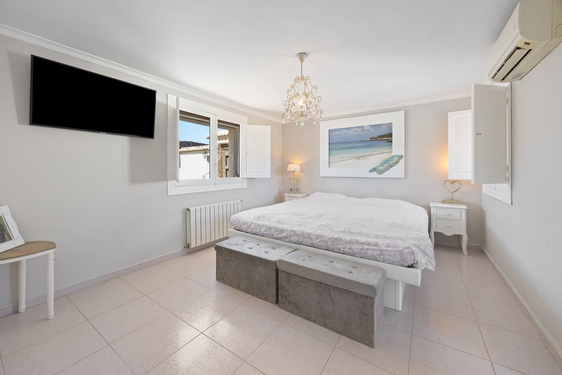 Dormitorio amplio con cama doble, contraventanas blancas y aire acondicionado. Incluye radiador, televisión de pared y suelos de gres en tonos neutros.