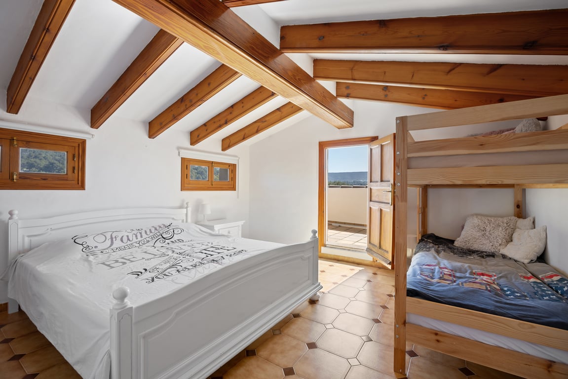 Dormitorio en el altillo con vigas de madera a la vista, suelos de terracota y acceso directo a una terraza privada. Incluye una cama doble y literas de madera.
