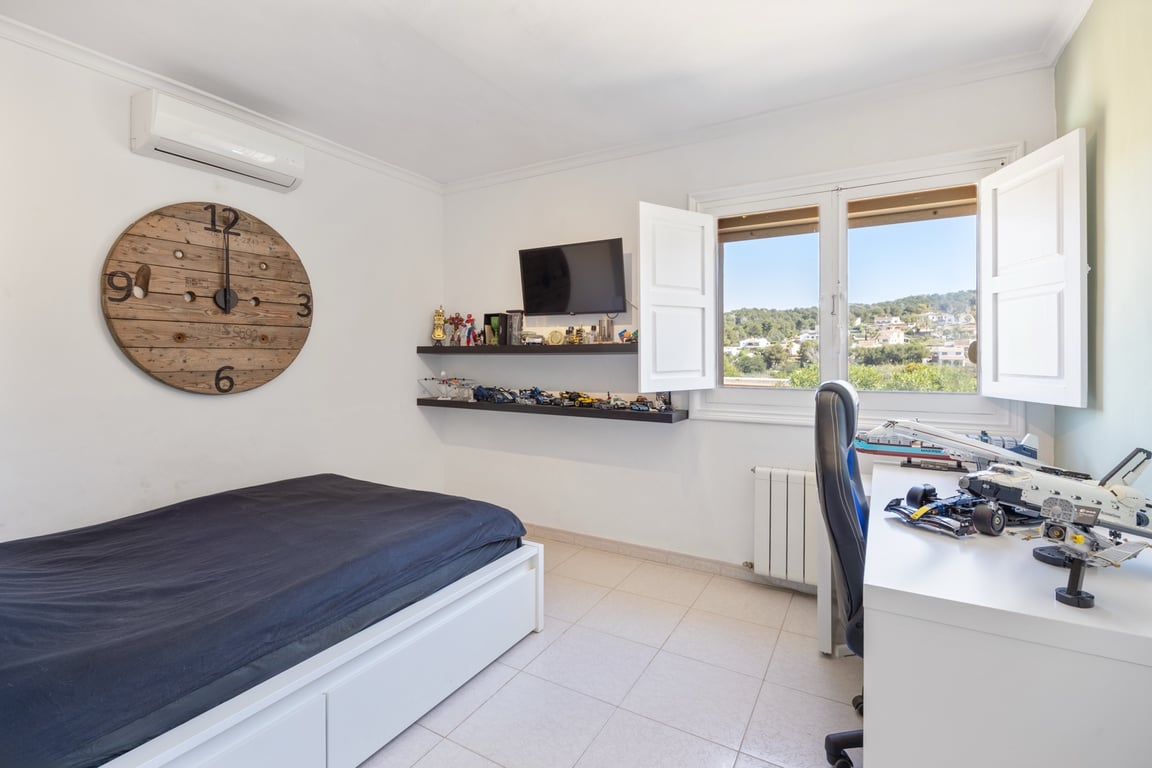 Dormitorio luminoso con aire acondicionado, escritorio de trabajo y ventana con contraventanas blancas que ofrece vistas despejadas al paisaje.