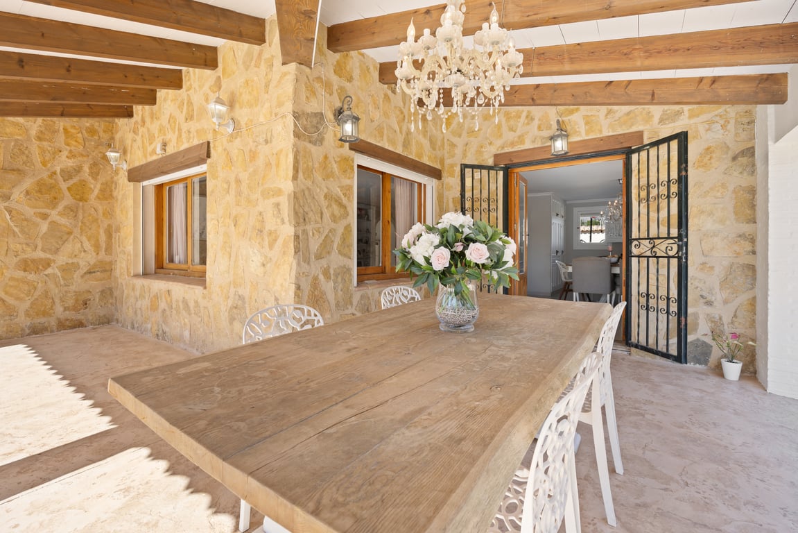 Naya cubierta con paredes de piedra natural, vigas de madera vista y una amplia mesa de comedor bajo una elegante lámpara de araña.
