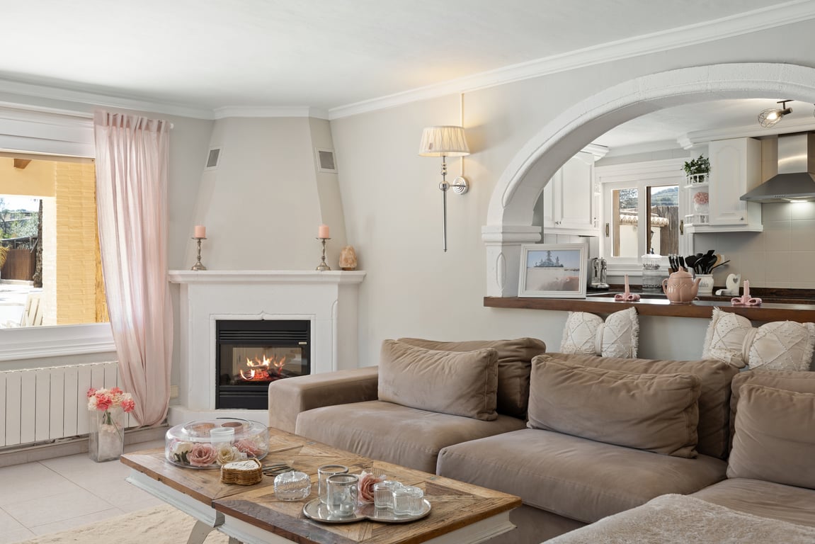 Salón luminoso con chimenea de esquina, sofá modular en tonos neutros y un arco decorativo que conecta visualmente con la cocina equipada.