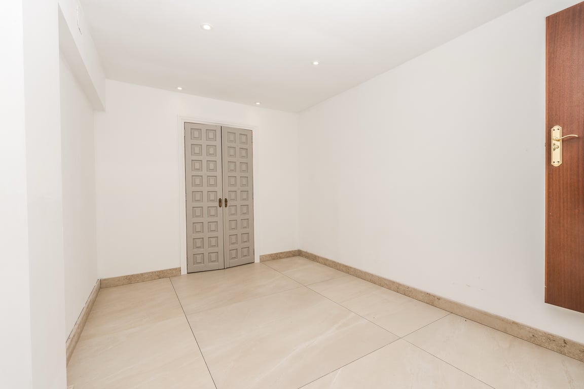 Habitación diáfana con suelos de mármol de gran formato, iluminación empotrada y puertas dobles decorativas con un distintivo diseño geométrico en gris.