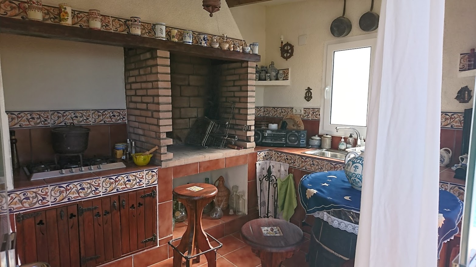Cocina de verano rústica con barbacoa de obra en ladrillo, encimeras de azulejo tradicional, armarios de madera y zona de cocción a gas integrada.