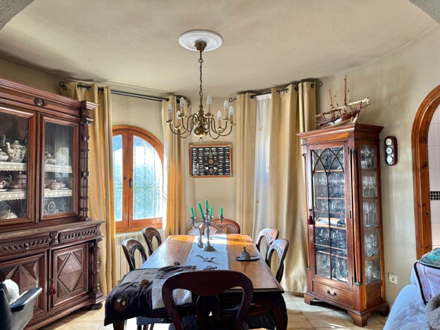 Comedor de estilo tradicional con mobiliario de madera maciza, vitrinas clásicas y luz natural a través de un ventanal de arco con carpintería de madera.