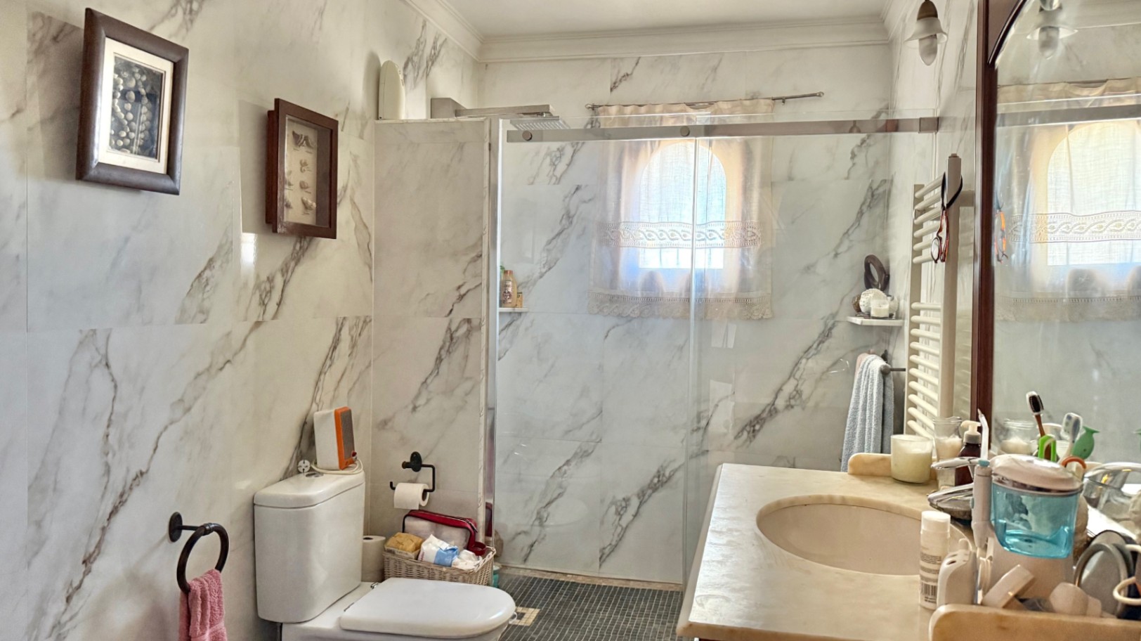 Cuarto de baño con paredes revestidas en mármol veteado, ducha a ras de suelo con mampara de cristal y ventana de arco que aporta luz natural.