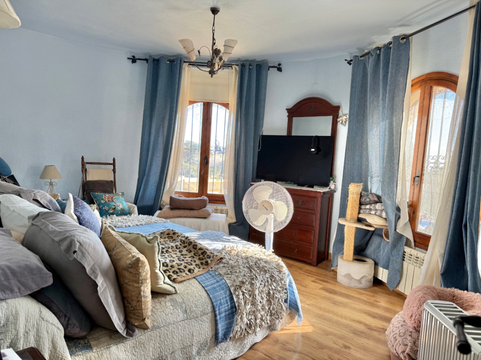 Dormitorio luminoso con paredes curvas, ventanas de madera en arco y suelos de tarima. Incluye mobiliario clásico de madera y abundante luz natural.