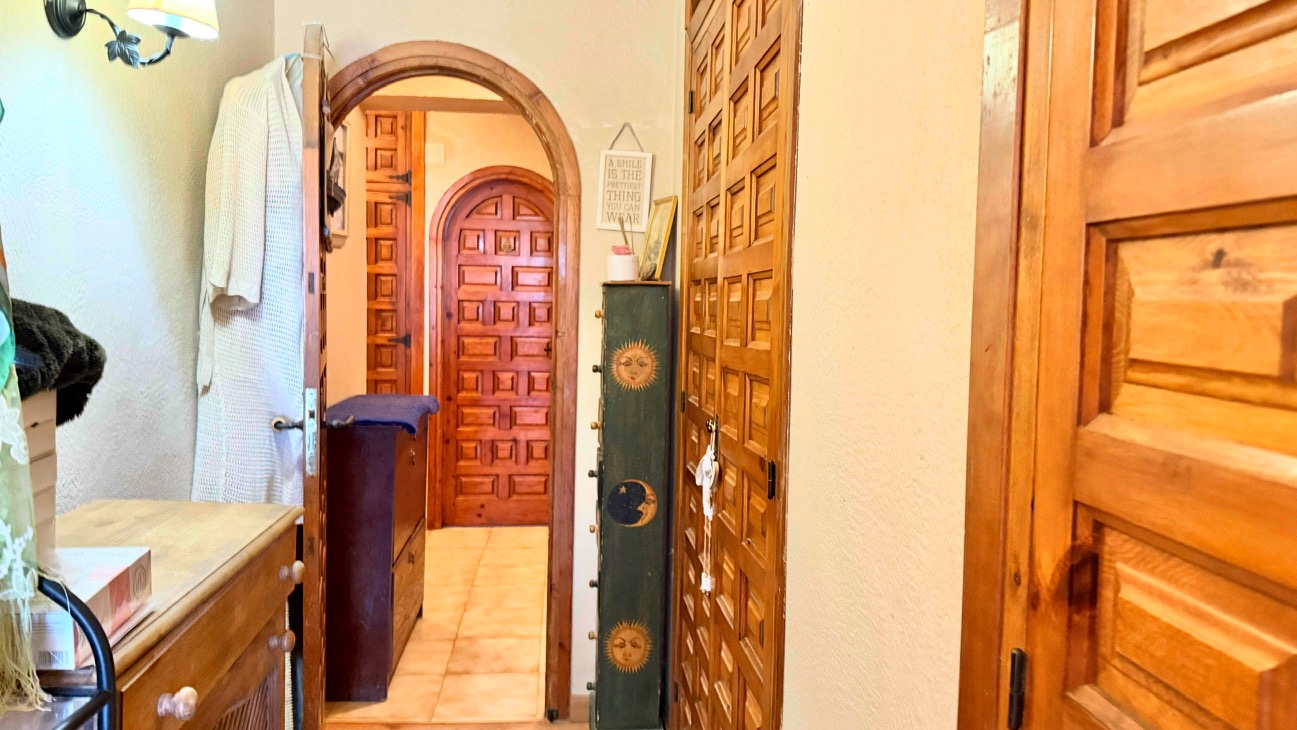 Pasillo con arcos de madera tradicionales y puertas de madera maciza con cuarterones, suelos de gres claros y luz natural suave.
