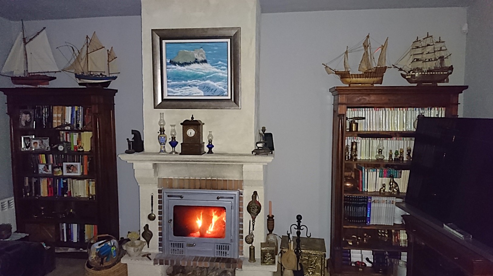 Salón con chimenea de leña encastrada, flanqueada por librerías de madera oscura decoradas con maquetas de barcos y elementos náuticos.