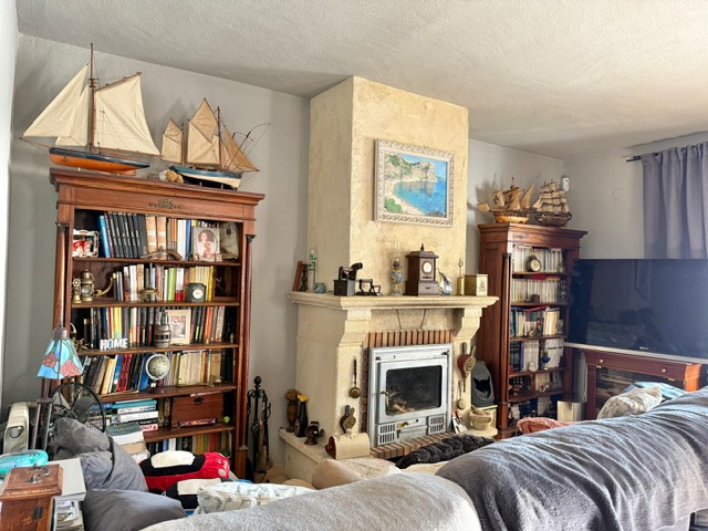 Salón tradicional con chimenea de piedra y casete metálico, flanqueada por librerías de madera clásica con decoración náutica y una amplia colección de libros.