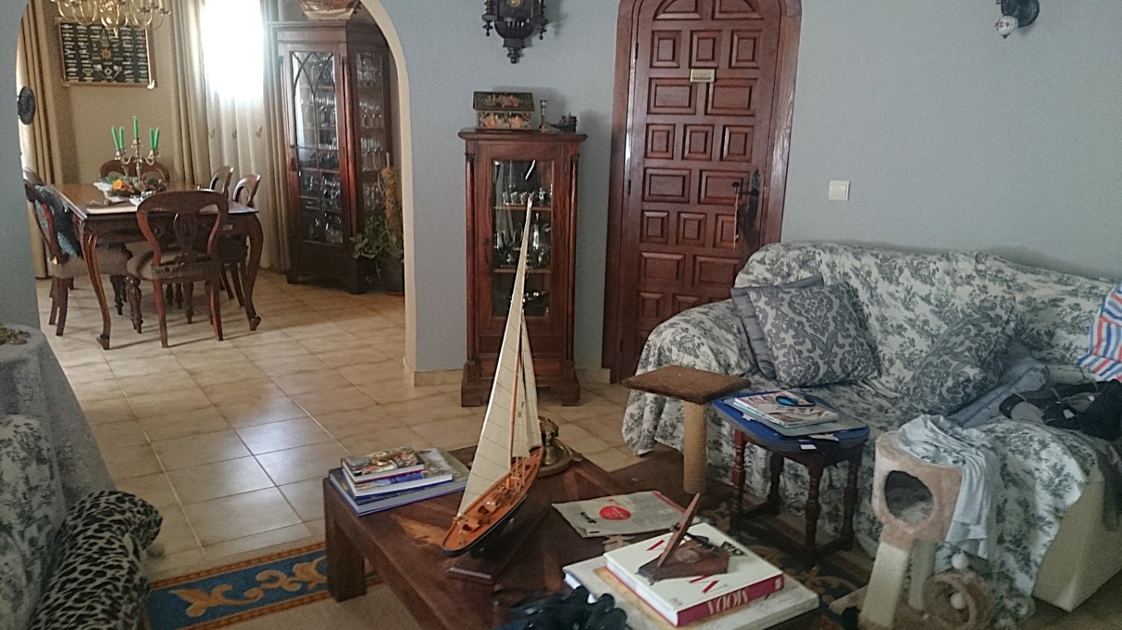 Salón tradicional con suelos de gres, mobiliario de madera clásica y un arco que conecta con el comedor. Incluye una puerta de madera tallada con remate redondeado.
