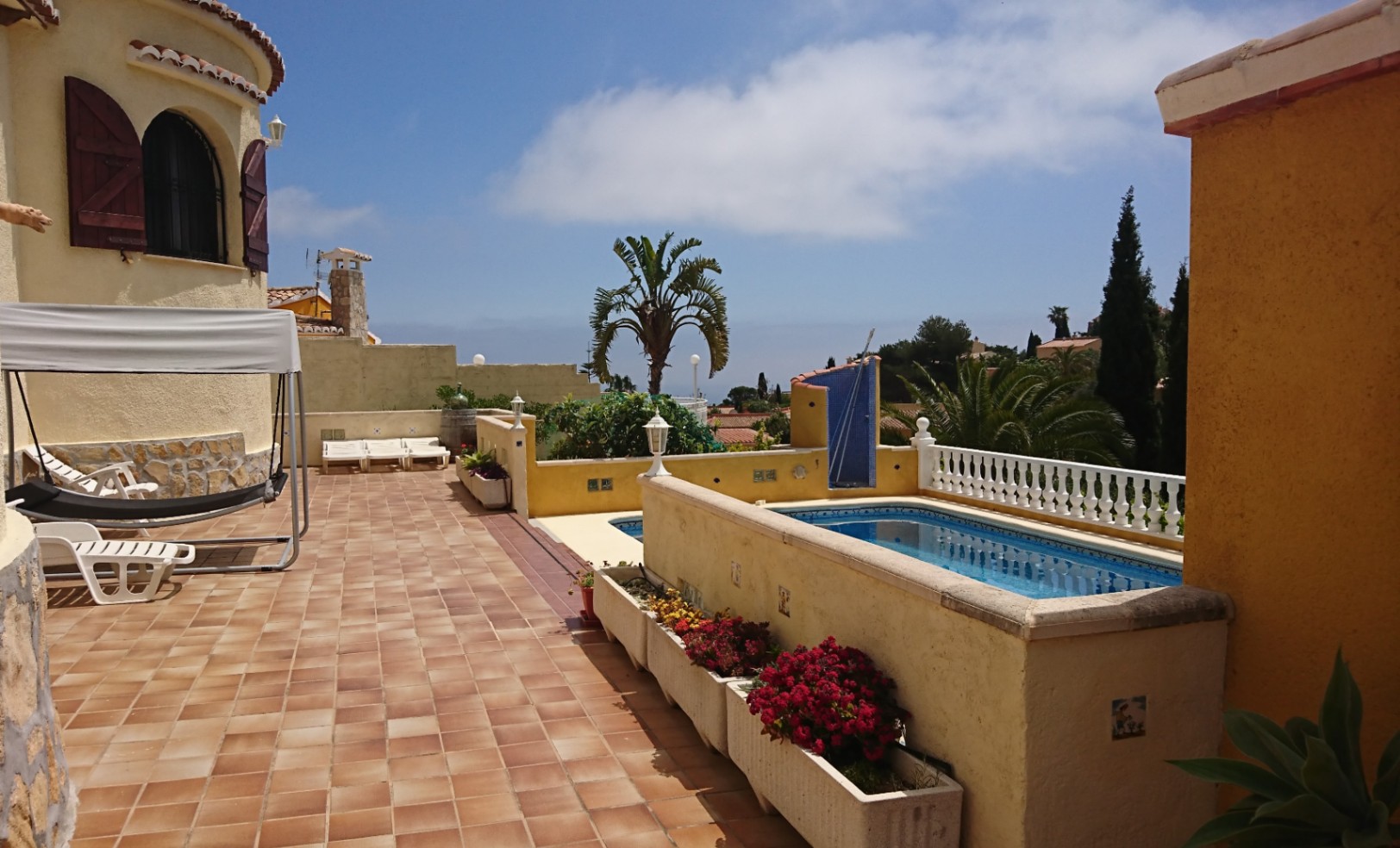 Terraza exterior con suelos de terracota, piscina privada con balaustrada blanca y zona de relax junto a la fachada de la villa con su torre característica.
