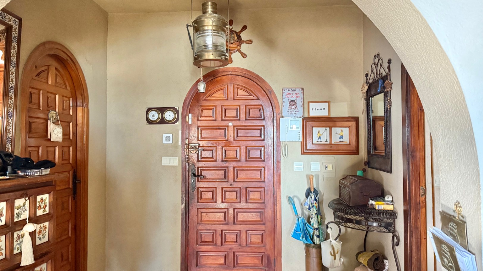 Vestíbulo de entrada con puertas de madera maciza en arco, decoración de temática náutica y una lámpara de latón suspendida.