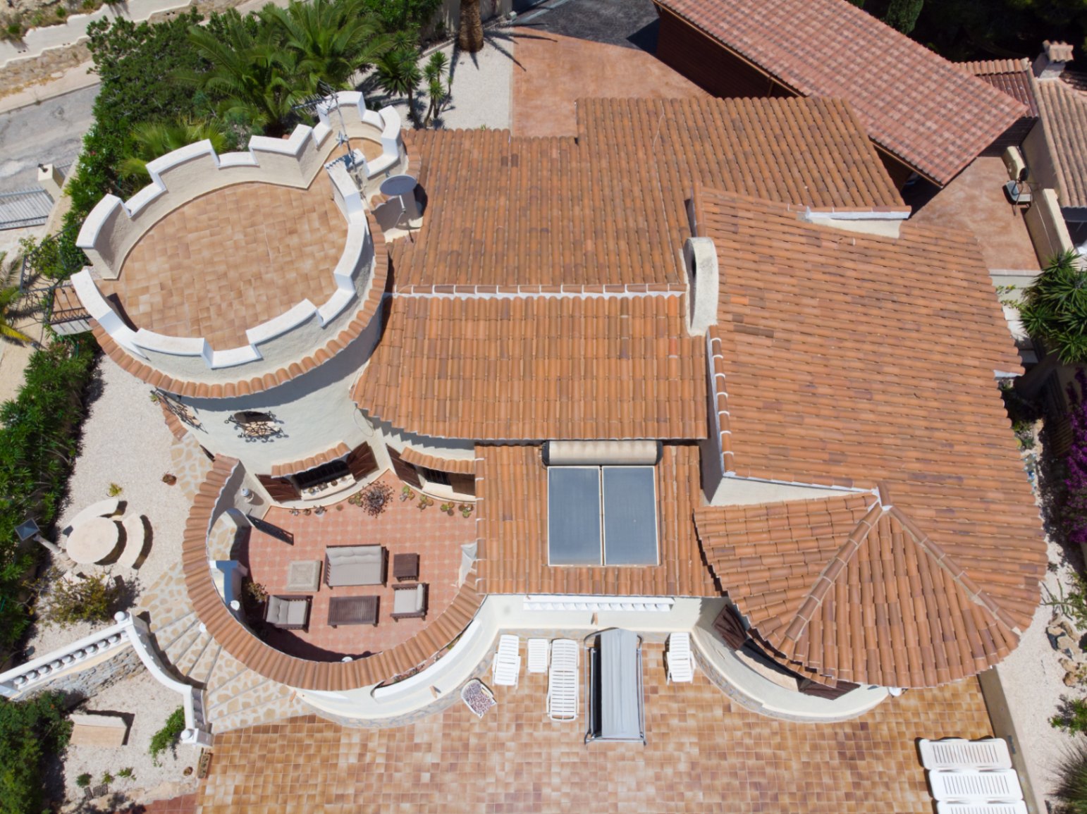 Vista aérea de la villa destacando su arquitectura mediterránea, la torre circular con almenas y las amplias terrazas de terracota con mobiliario exterior.