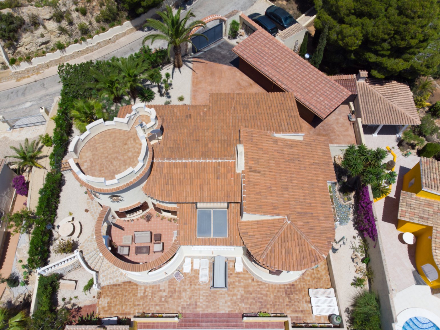 Vista aérea de la villa que muestra su arquitectura mediterránea con techos de teja, una torre distintiva, paneles solares y amplias terrazas exteriores.