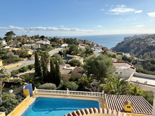 Vista panorámica desde la terraza superior que muestra la piscina privada con balaustrada blanca, el entorno residencial de Benitachell y el mar Mediterráneo al fondo.