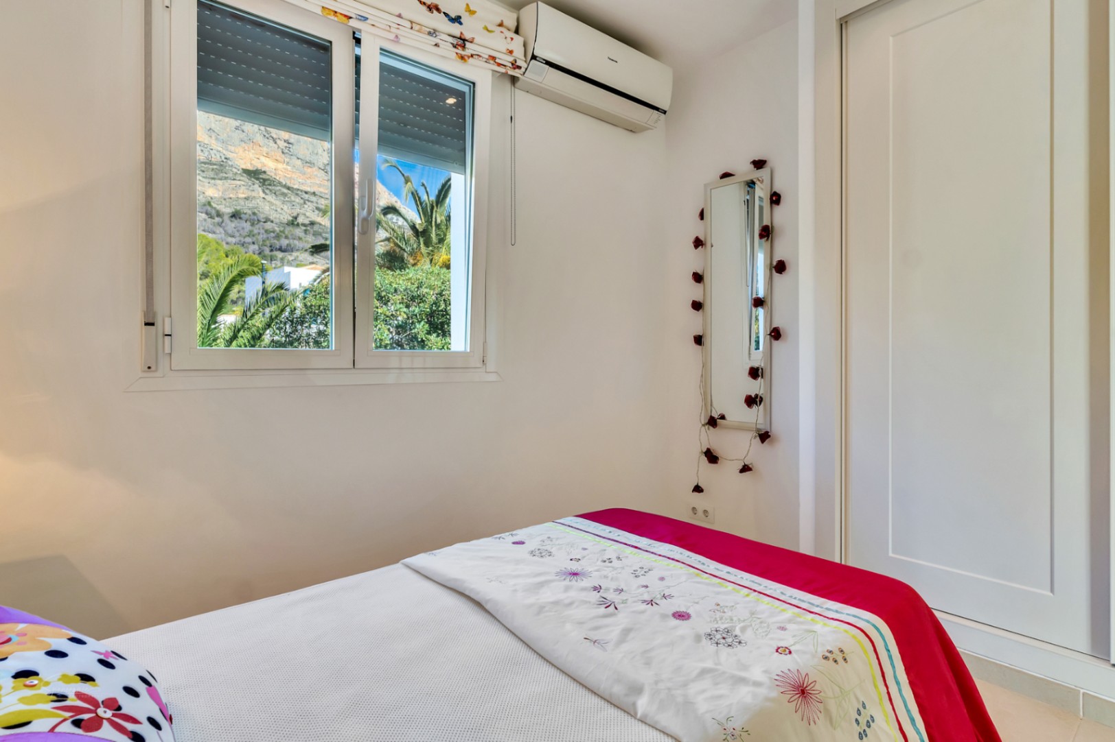 Dormitorio luminoso con aire acondicionado, armario empotrado blanco y ventana con vistas directas al macizo del Montgó y vegetación mediterránea.