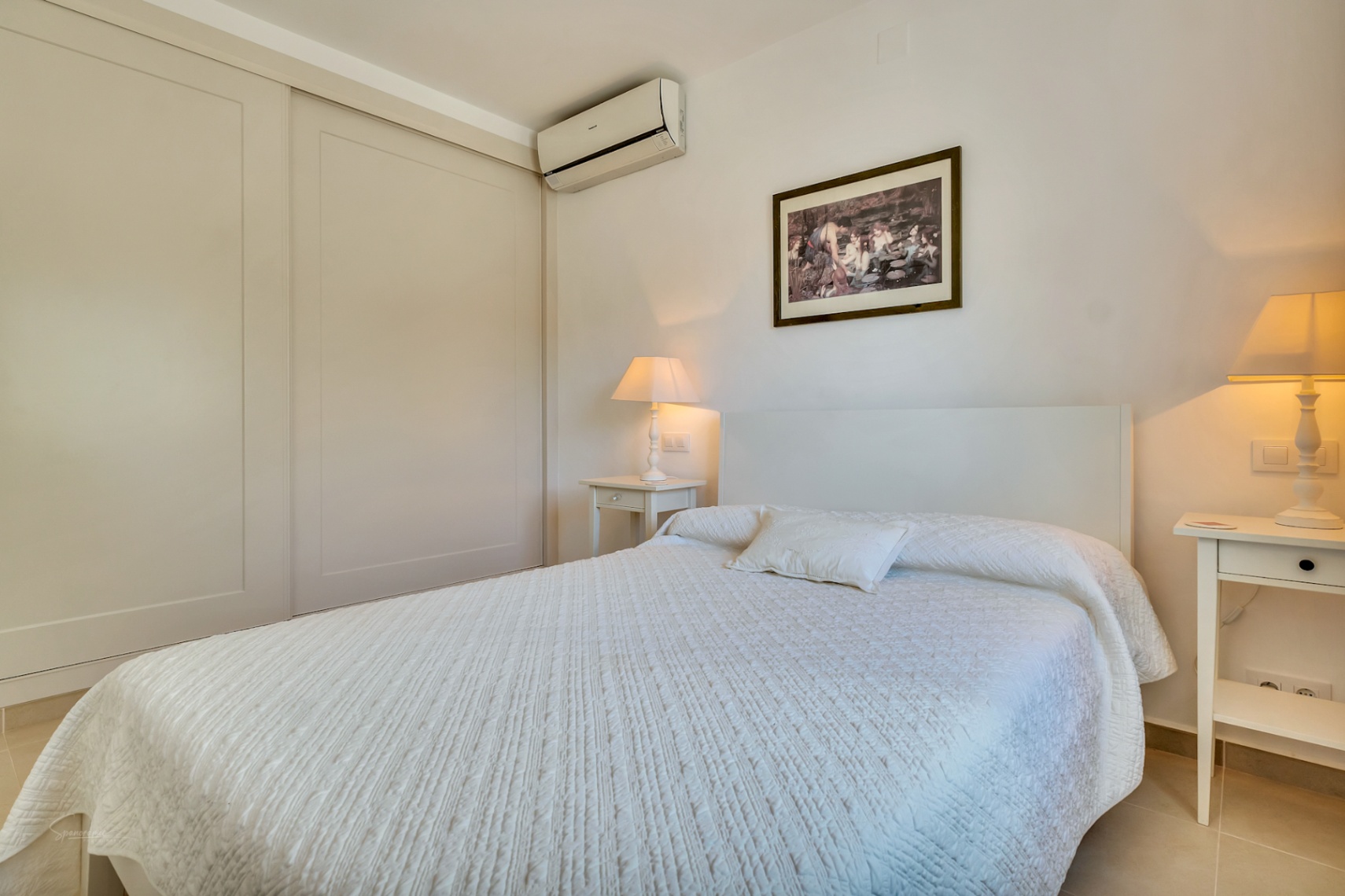 Dormitorio luminoso con armarios empotrados de puertas correderas, aire acondicionado y mesitas de noche a juego con lámparas de luz cálida.