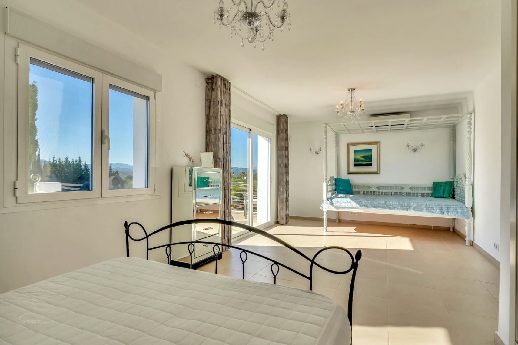 Dormitorio principal luminoso con cama de forja, zona de estar con diván de madera blanca y acceso directo a la terraza con vistas al Montgó.